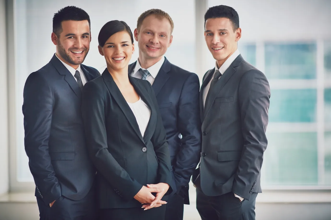 Professional business team smiling in suits, standing together in a modern office
